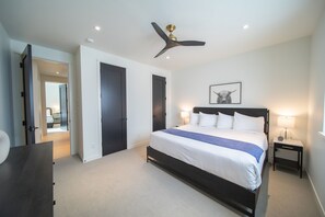 Une chambre à coucher moderne avec un grand lit, un ventilateur de plafond et une table de chevet avec une lampe.