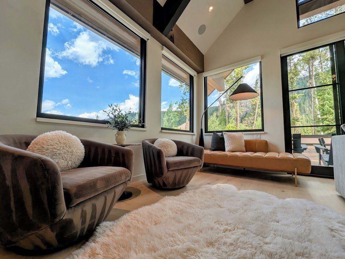 A modern living room with large windows, a sofa, two armchairs, and a fluffy rug.