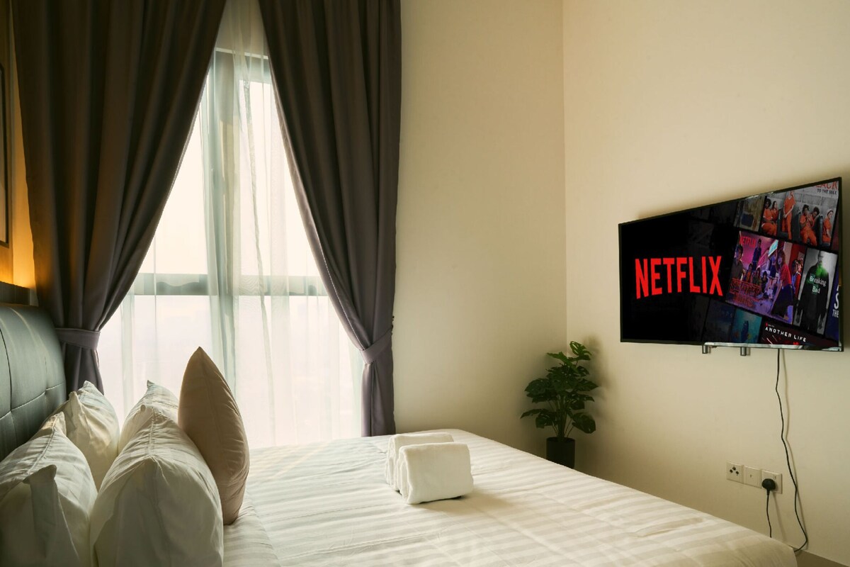 Ein Hotelzimmer mit Bett, Fernseher mit Netflix-Anzeige, einem Fenster mit Vorhängen und einer Pflanze.