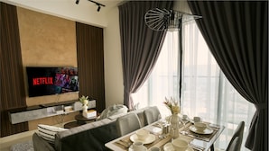 A modern living room with a flat-screen TV displaying Netflix, a dining area with a set table, and a large window with curtains. - Trion Kuala Lumpur by Roam (Kuala Lumpur)