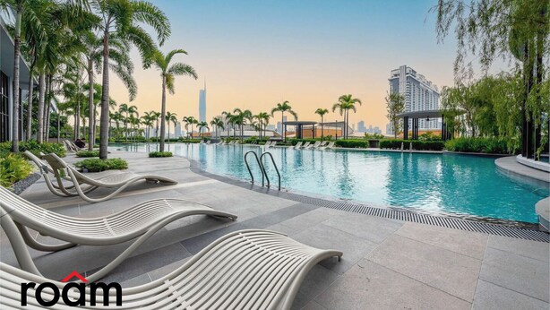 A modern pool area with lounge chairs, palm trees, and a view of a city skyline. - Trion Kuala Lumpur by Roam (Kuala Lumpur)