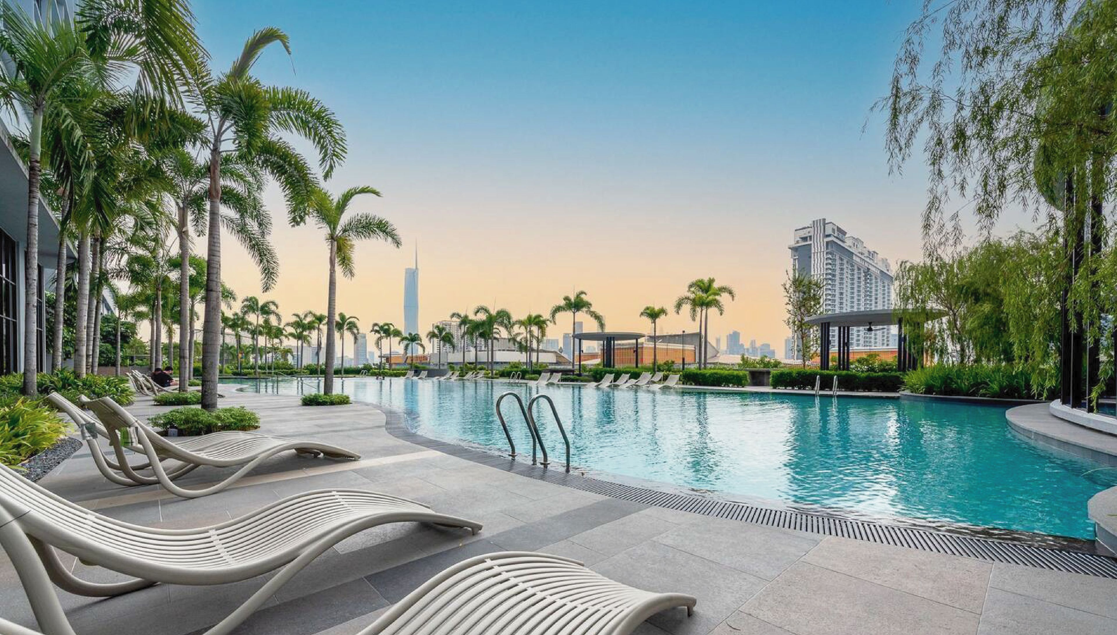 Uma área de piscina moderna com espreguiçadeiras, palmeiras e vista para o horizonte urbano.