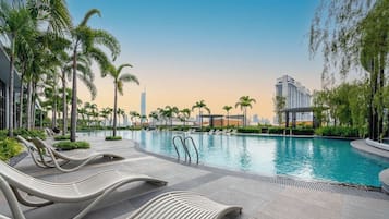 Uma área de piscina moderna com espreguiçadeiras, palmeiras e vista para o horizonte urbano.