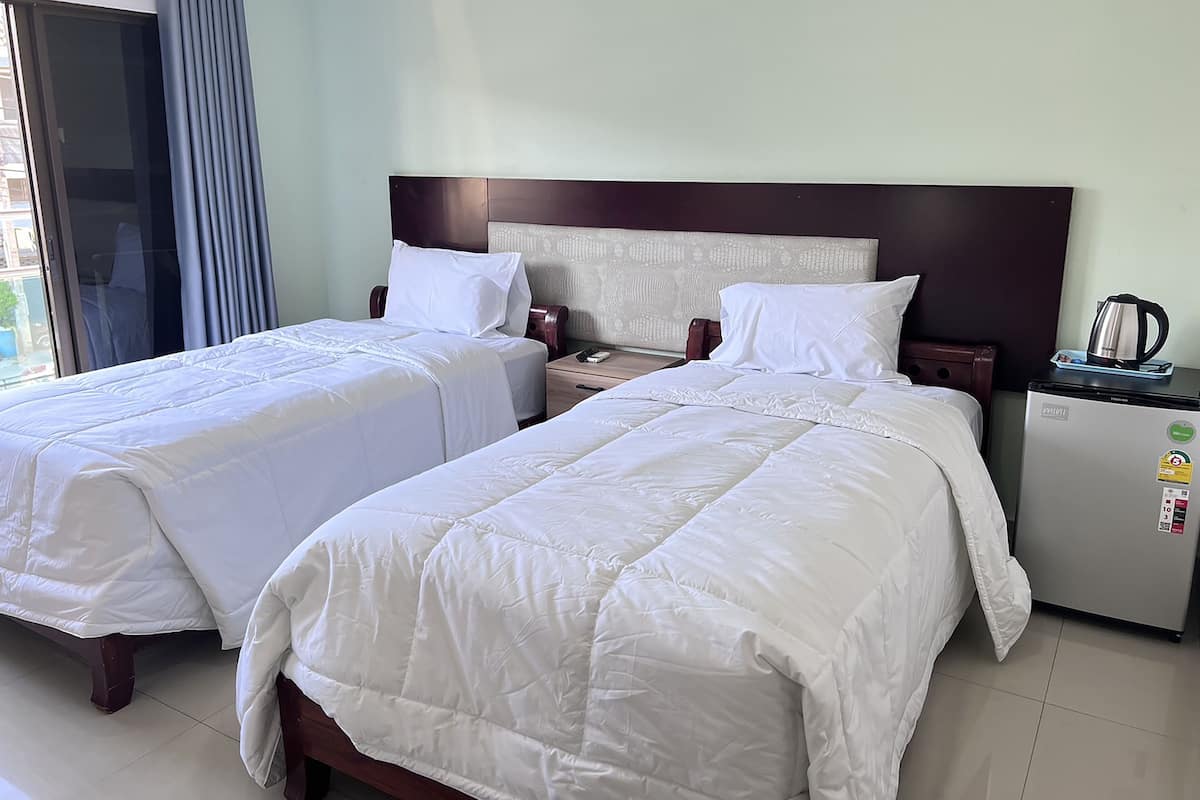 Habitación de hotel con dos camas, una mesita de noche, un refrigerador y una ventana con cortinas.