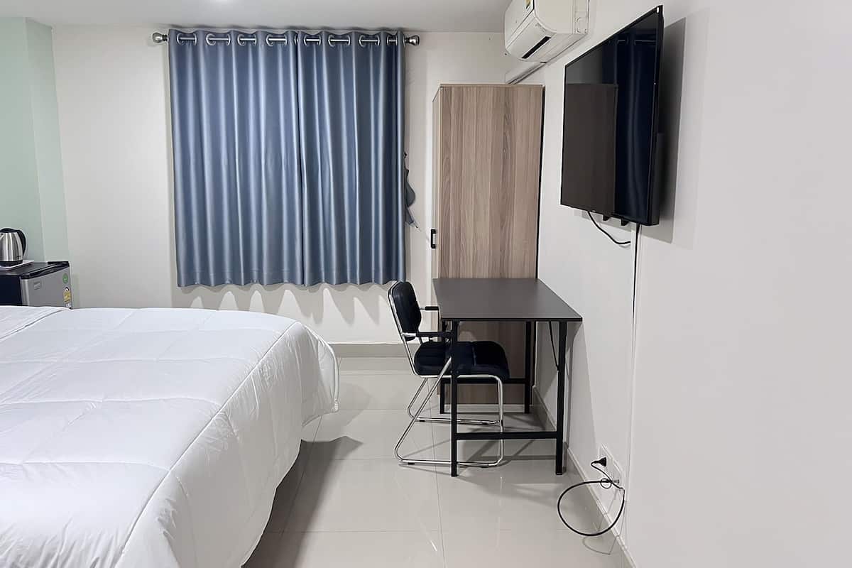 Una habitación de hotel con cama, escritorio, silla, televisor y aire acondicionado.