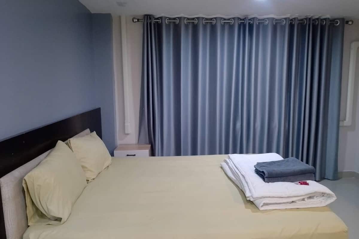 Una cama bien hecha con almohadas, una toalla doblada y una mesita de noche con lámpara.