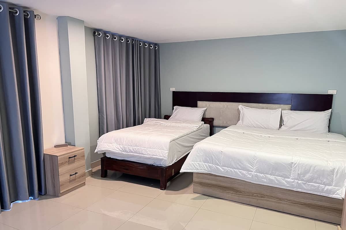 Una habitación de hotel con dos camas, una mesita de noche de madera y un pequeño aparador.