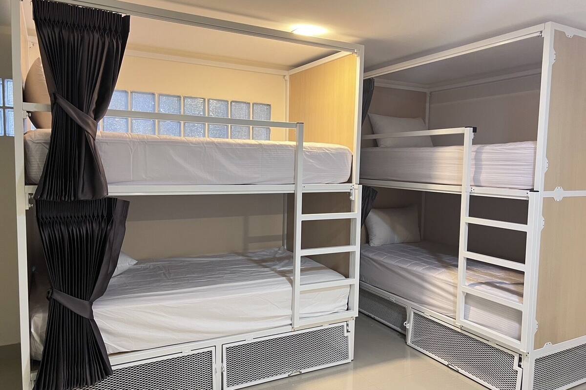 Habitación con literas, una cortina, un ventanal y una cama con colchón blanco.