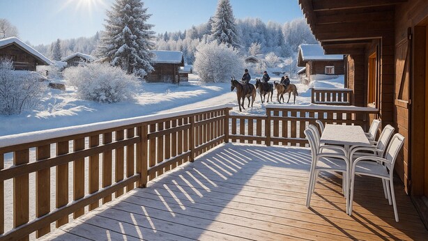 A wooden deck with chairs and a table, overlooking a snowy landscape with houses and horses.