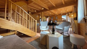 A wooden cabin interior with a staircase, seating area, and a dining table.