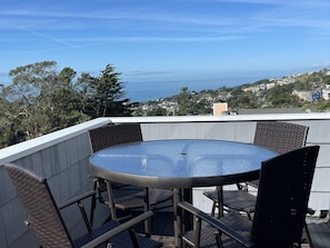 A round table with wicker chairs on a rooftop terrace with a view of the ocean and hills. - Sea Breeze with Ocean View Balconies | 3BD/2.5BA (Pacifica)