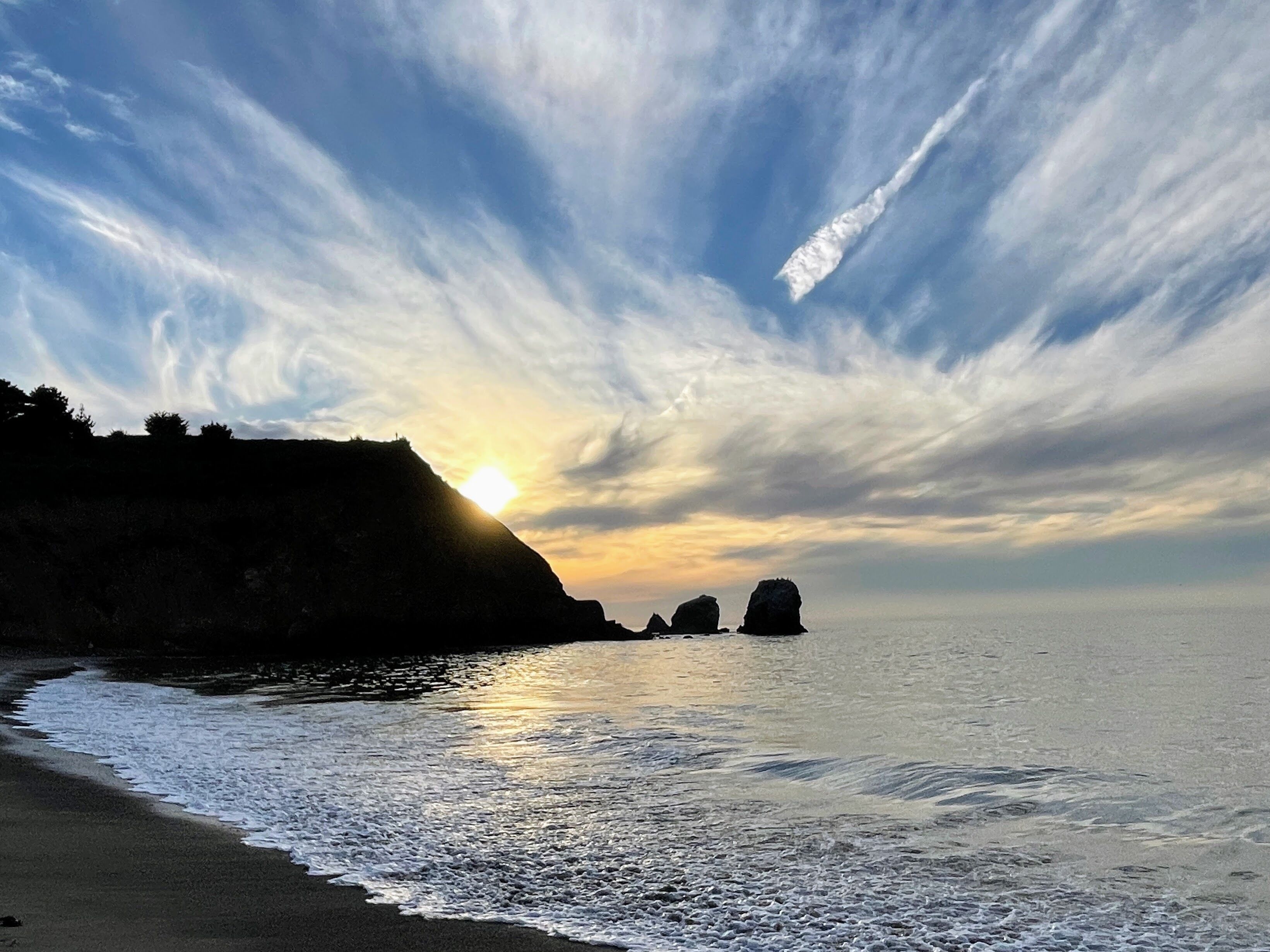 A beach with calm waters, a clear sky, and a sunset.