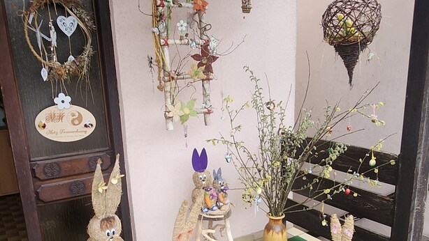 Un ingresso decorato con una porta in legno, un tappetino verde e diverse decorazioni pasquali, tra cui un coniglio, uova e una gabbia per uccelli appesa.