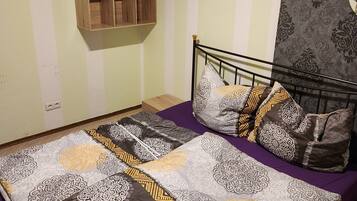 A bedroom with a bed, pillows, a wall-mounted shelf, and a patterned wall.