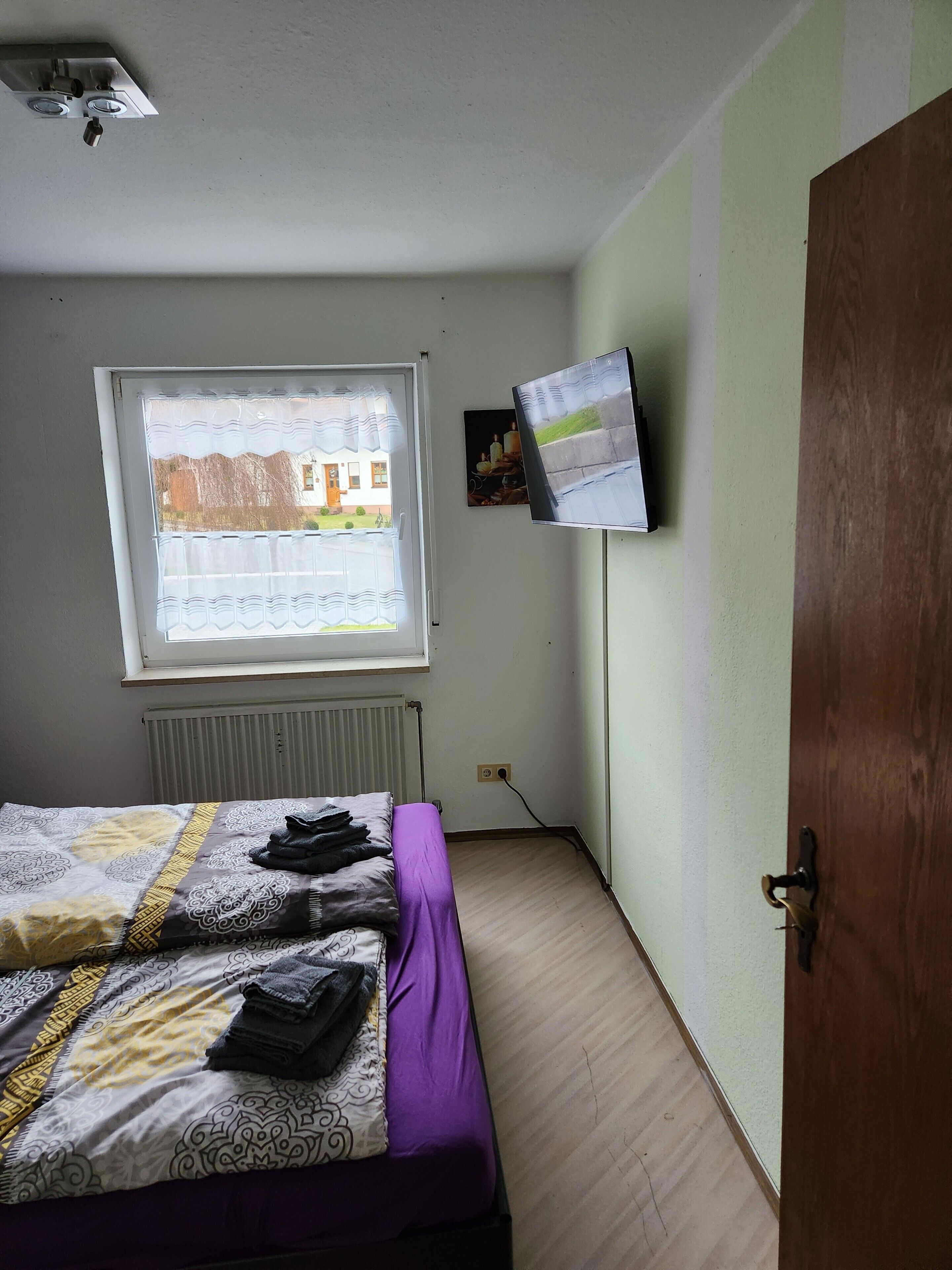 Un dormitorio con una cama, una ventana, un televisor de pared y un radiador.
