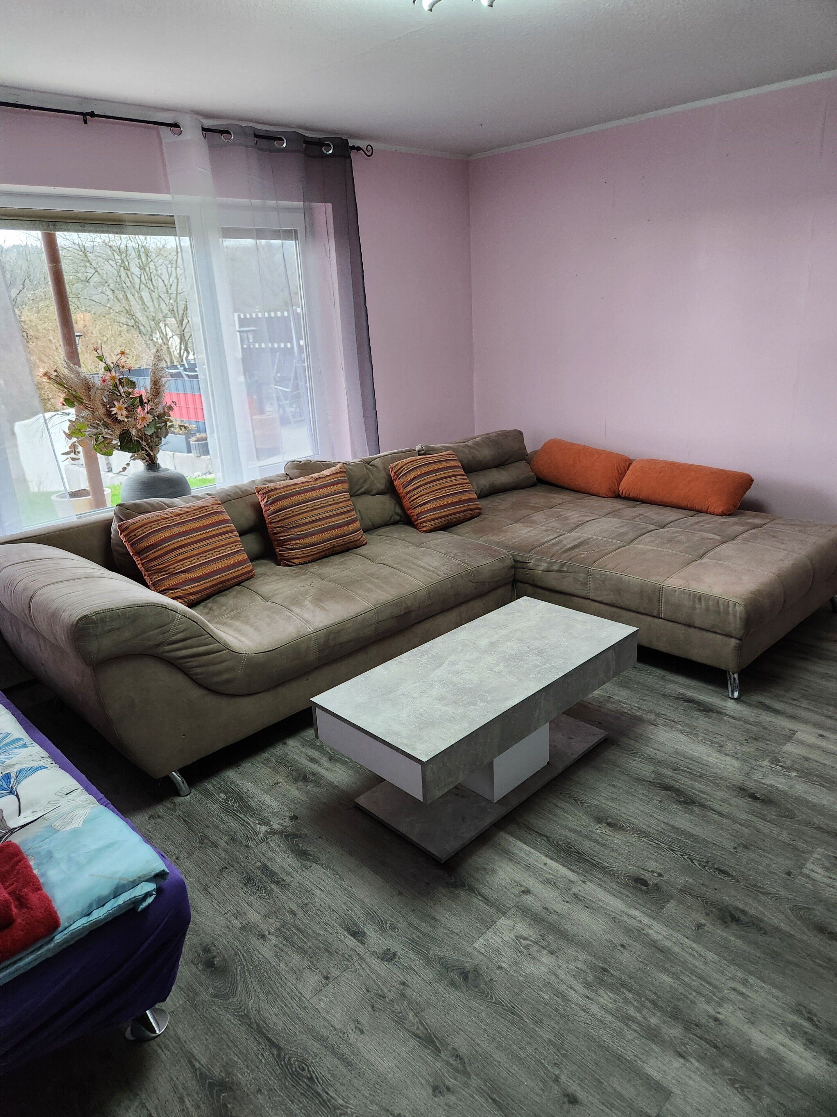 A living room with a sectional sofa, a coffee table, and a view through a window.