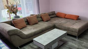 A living room with a sectional sofa, a coffee table, and a view through a window.