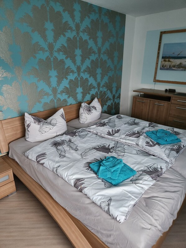 A bedroom with a bed, wooden headboard, patterned wall, and a painting on the wall.