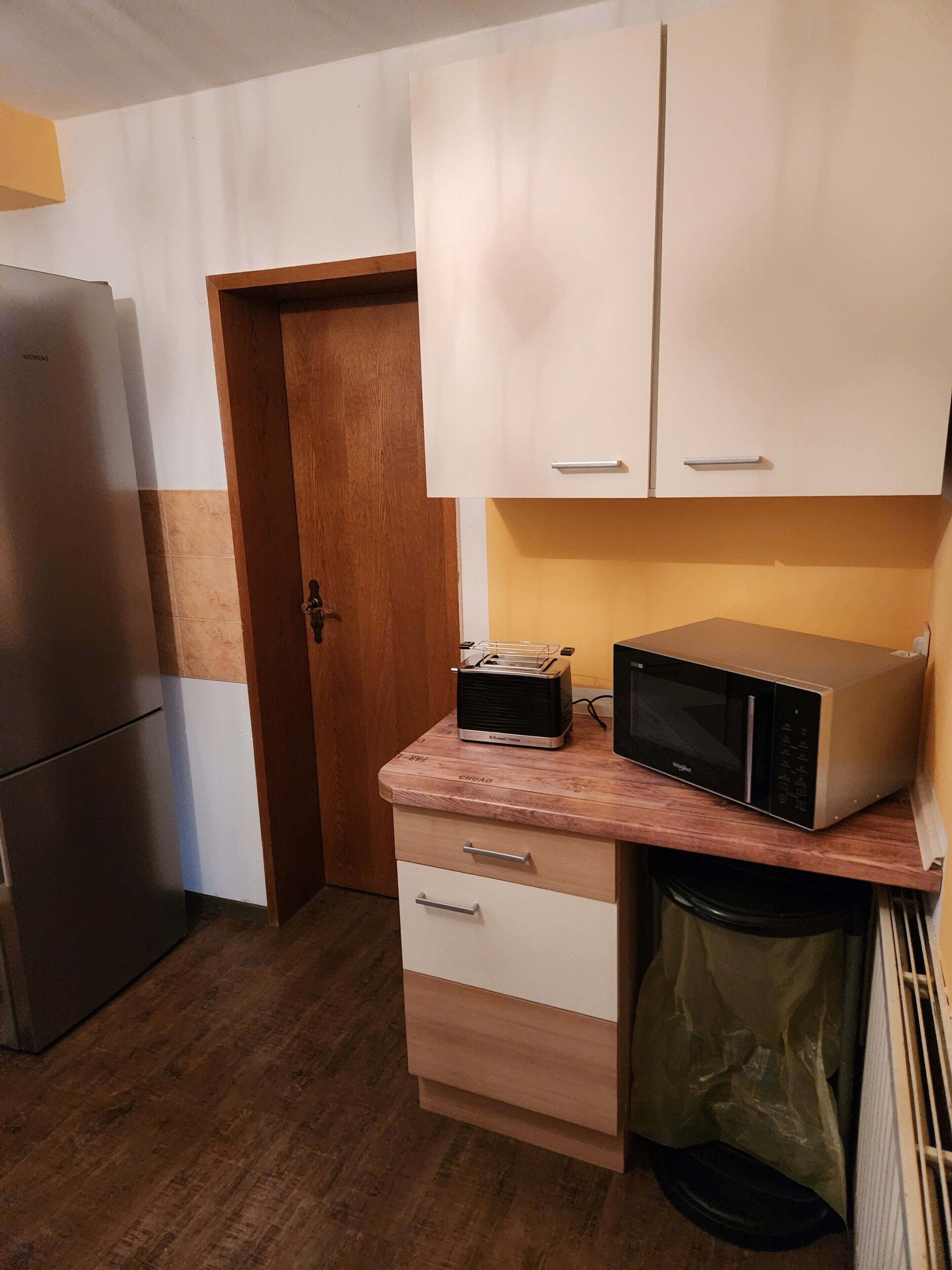 A compact kitchen with a refrigerator, microwave, and wooden countertop drawers.