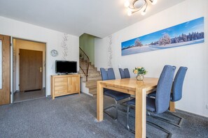 Ein Essbereich mit Holztisch und Stühlen, einem Fernseher auf einer Kommode, einer Treppe und einem Wandbild mit Winterlandschaft.