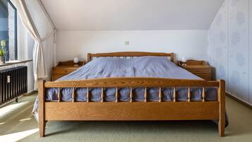 Ein Schlafzimmer mit einem hölzernen Bett, einem Nachttisch, einer Lampe und einem Fenster mit Vorhängen.