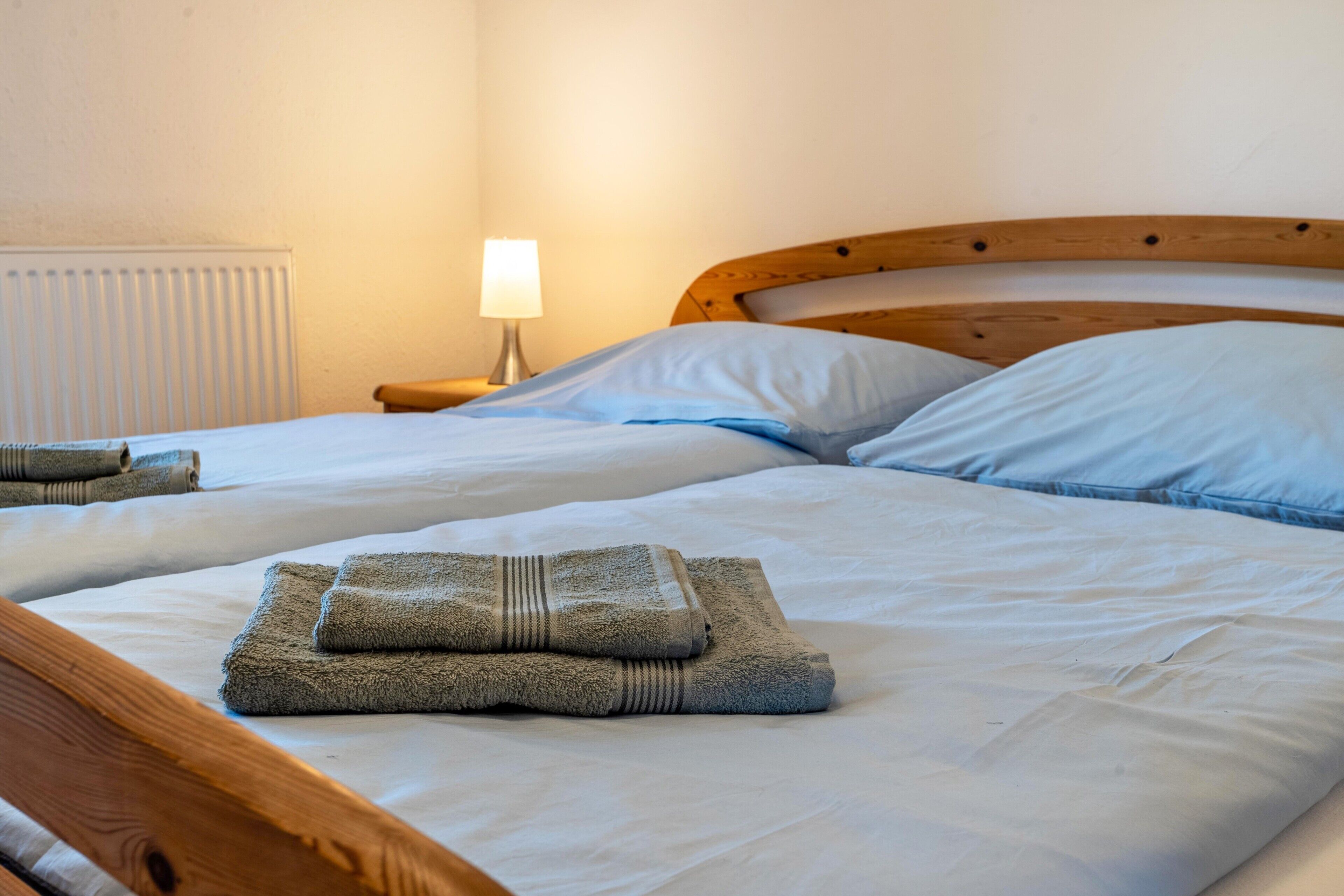 Ein Doppelbett mit Holz-Kopfteil, zwei Kissen, einer Nachttischlampe und gefalteten Handtüchern auf dem Bett.