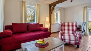 A red sofa, a plaid armchair, and a wooden coffee table with fruit. - Apartment 'Hof Verchen Nahe Kummerower See' with Private Terrace, Private Garden and Wi-Fi (Verchen)