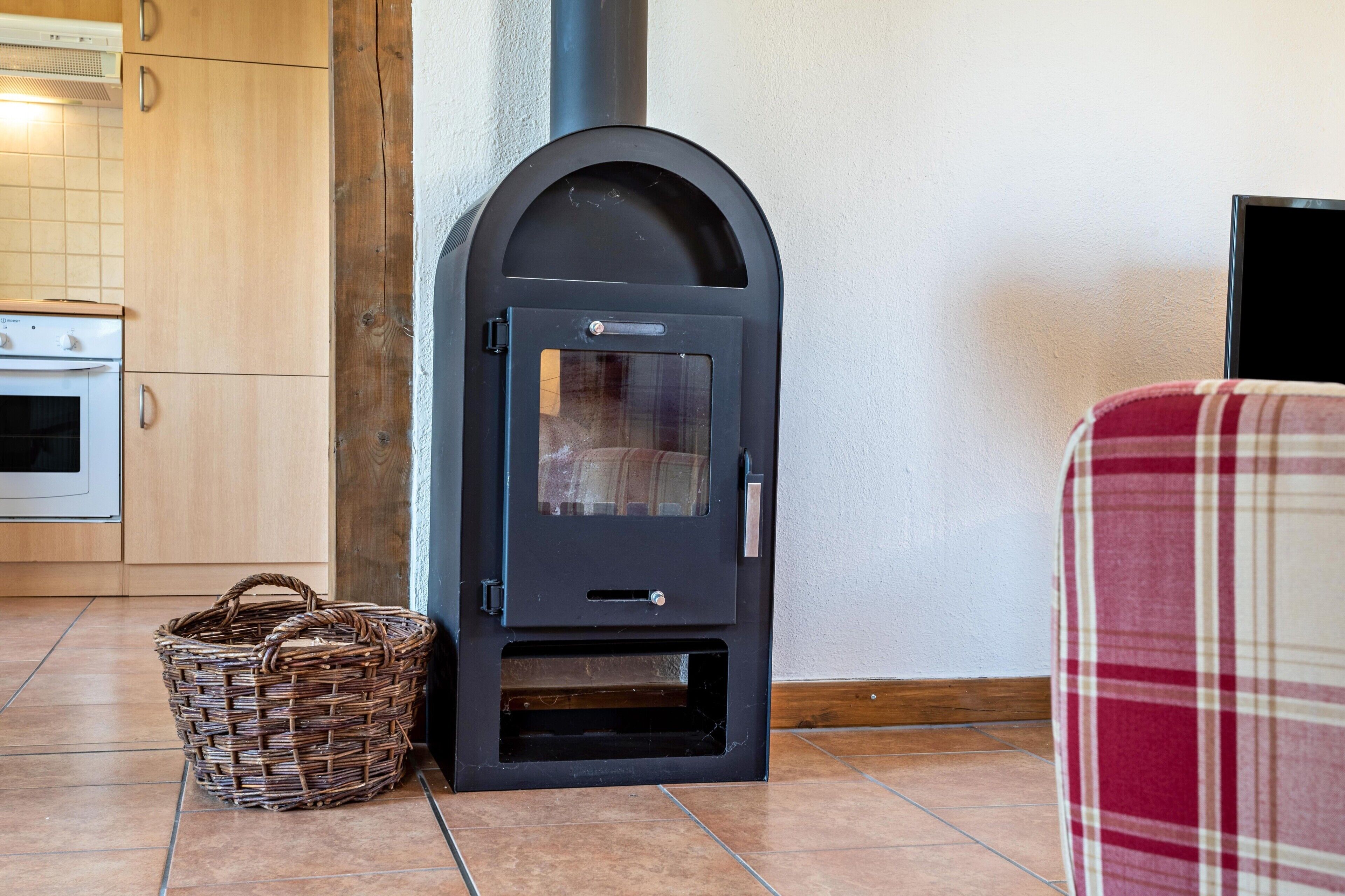 A kitchen with a wood-burning stove, a wicker basket, and a plaid chair.