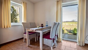 A dining area with a table and chairs, a window with curtains, and a view of a field. - Apartment 'Hof Verchen Nahe Kummerower See' with Private Terrace, Private Garden and Wi-Fi (Verchen)