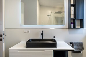 A bathroom with a rectangular black sink, a mirror, a towel rack, and a shelf with toiletries. - Apartment 'City Villa Bad Dürrheim - Penthouse' with Balcony and Wi-Fi (Bad Dürrheim)