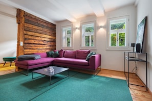 Een moderne woonkamer met een modulaire bank, een salontafel, een houten accentmuur en een groot raam met uitzicht op groen.