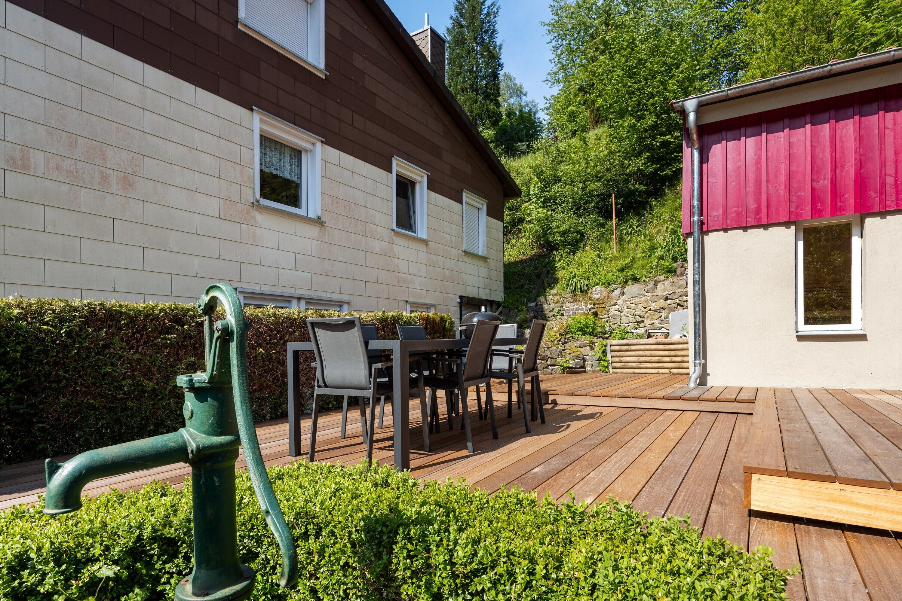 A wooden deck with outdoor furniture, a green fire hydrant, and a house with a red roof.