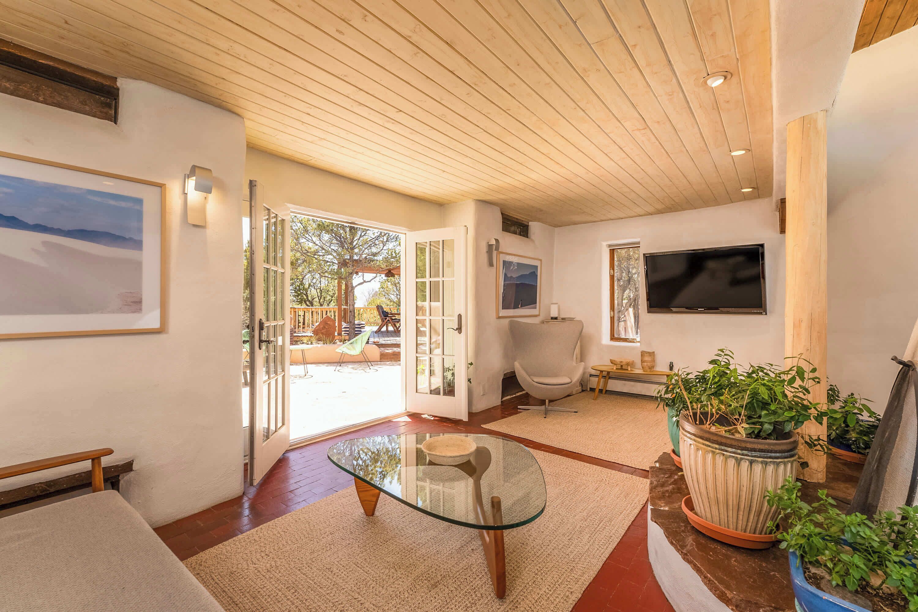 A spacious living area with a glass-top coffee table, a comfortable chair, a flat-screen TV, and a large window offering a view of the outdoors.