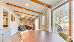 Un espace repas avec une table ronde et des chaises, des poutres en bois au plafond et une vue sur l’extérieur grâce à de grandes fenêtres.