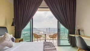 A hotel room with a bed, a desk, two chairs, and a balcony with a view of the city. - Datum Jelatek Sky Residence Roam (Ampang)