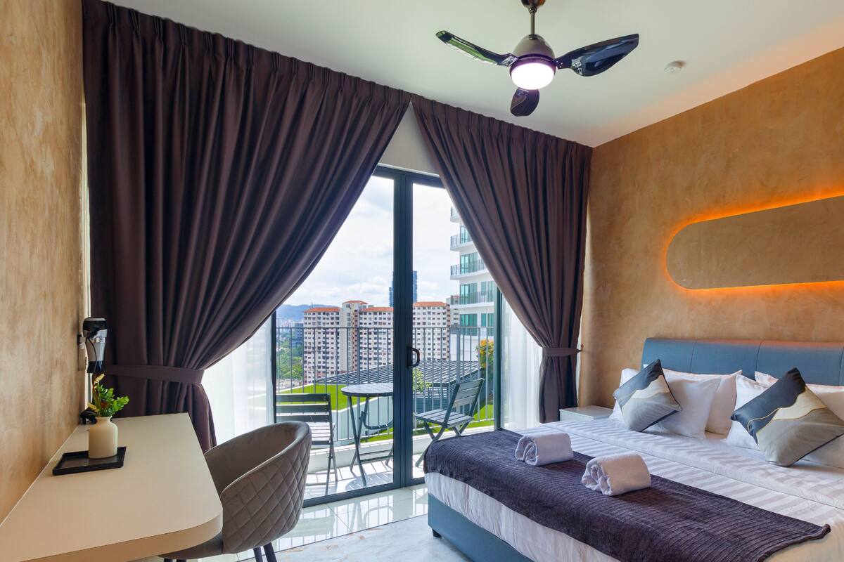 Ein modernes Hotelzimmer mit einem großen Bett, einem Schreibtisch und einem Stuhl. Ein Balkon bietet Blick auf die Stadt.