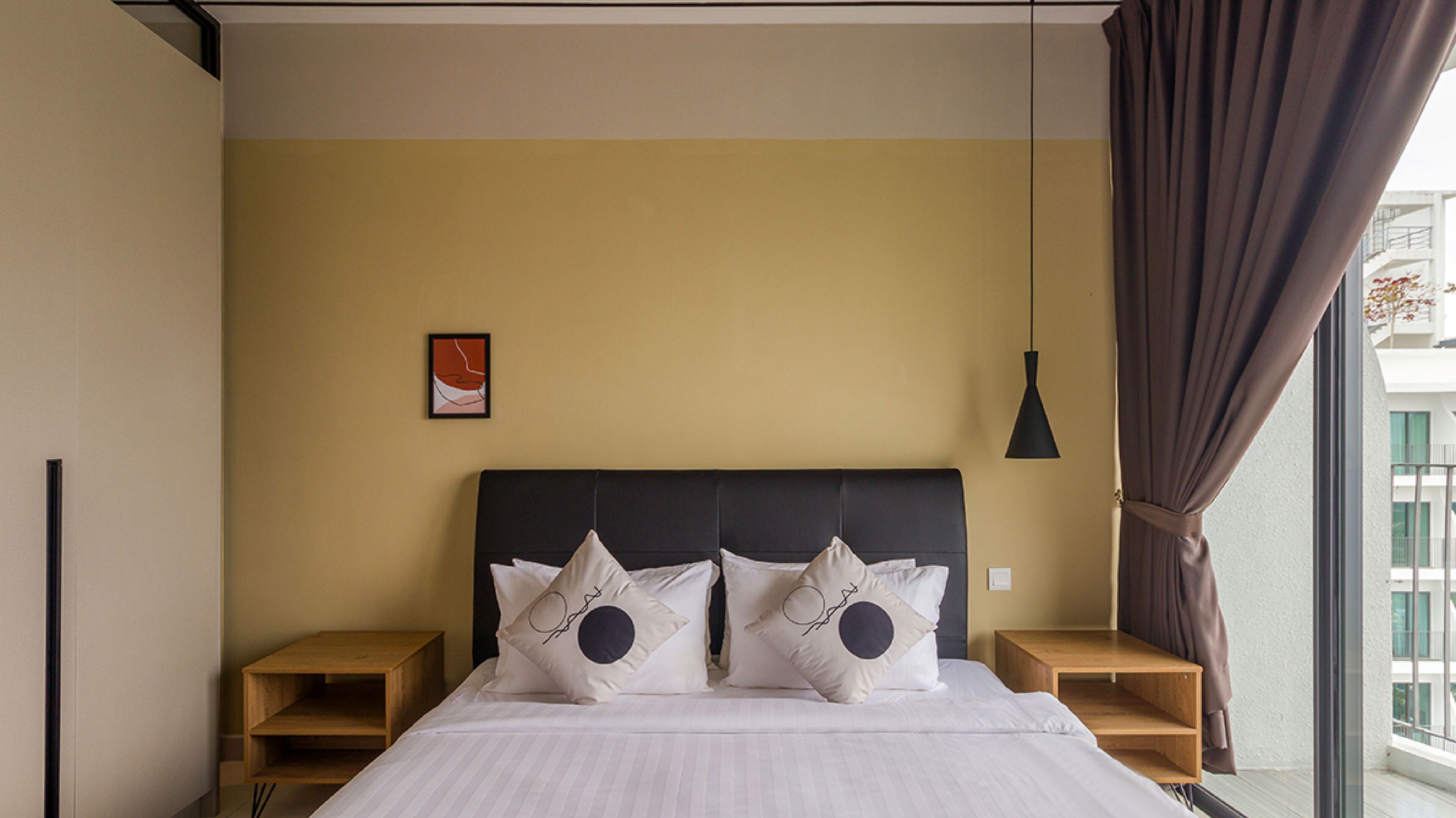 A hotel room with a large bed, two bedside tables, a hanging pendant light, and a view of the outside.