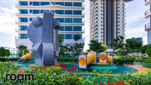 A playground with climbing structures and slides, surrounded by greenery and modern buildings. - Datum Jelatek Sky Residence Roam (Ampang)