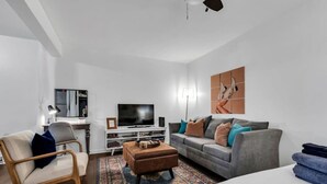 A modern living room with a sofa, armchair, TV, and artwork on the wall. - Near 12th South | Pool | 3 mi. to Broadway (Nashville)