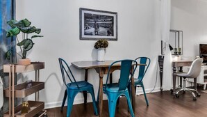 A modern office space with a wooden table, teal chairs, a framed picture on the wall, a potted plant, and a desk with a computer. - Near 12th South | Pool | 3 mi. to Broadway (Nashville)