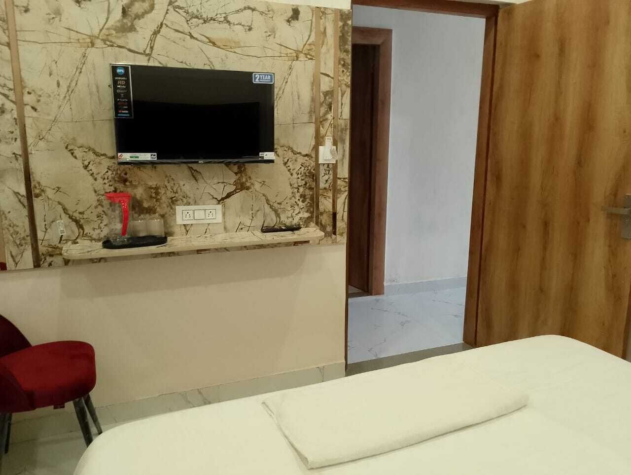 A hotel room with a bed, a TV mounted on the wall, a red chair, and a wooden door.