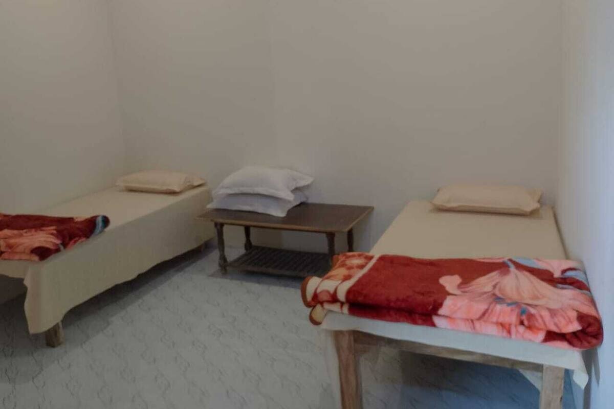 Una habitación con dos camas individuales, una mesita pequeña y un banco.