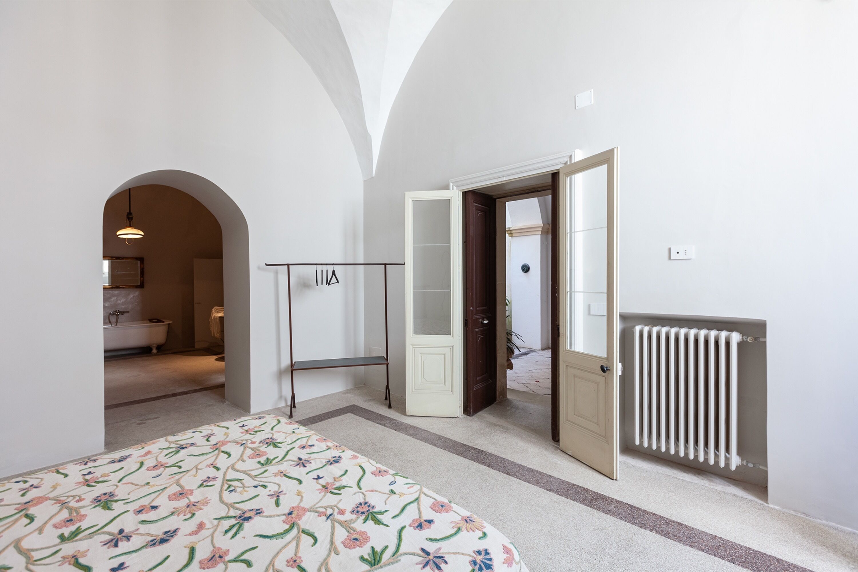 A bedroom with a bed, an open door to a bathroom, a radiator, and a hanging light fixture.