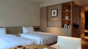 A hotel room with two beds, a wooden table with a tray, a white pitcher, and a framed picture on the wall.