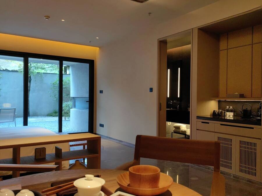 Quarto de hotel moderno com uma cama grande, uma mesa de jantar e vista para o exterior.