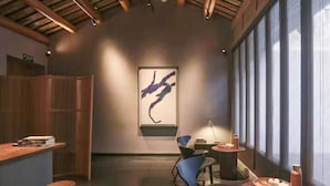 A modern interior with exposed wooden beams, a large abstract painting, and a view through large windows. - Jiangnan House Chaozhou (Chaozhou)