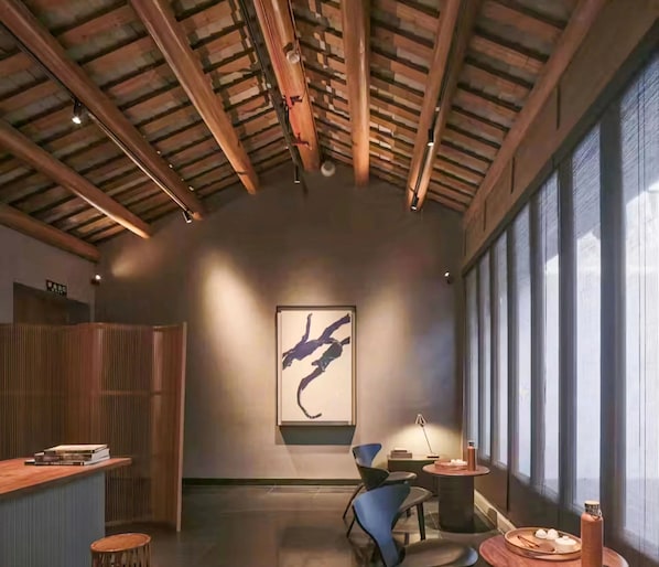 A modern interior with exposed wooden beams, a large abstract painting, and a view through large windows.