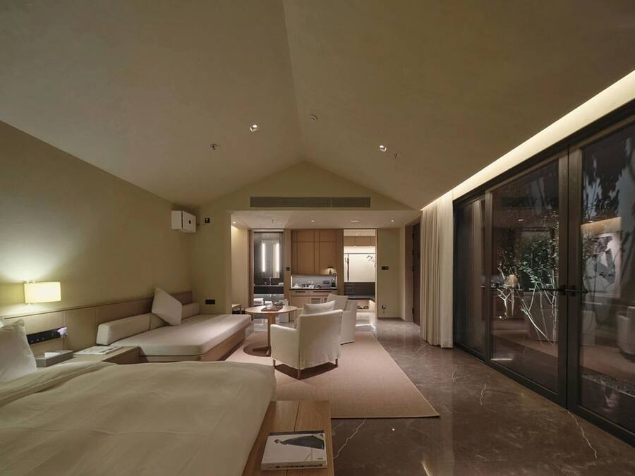 A modern hotel room with a large bed, a seating area, a kitchen, and a balcony with a view.