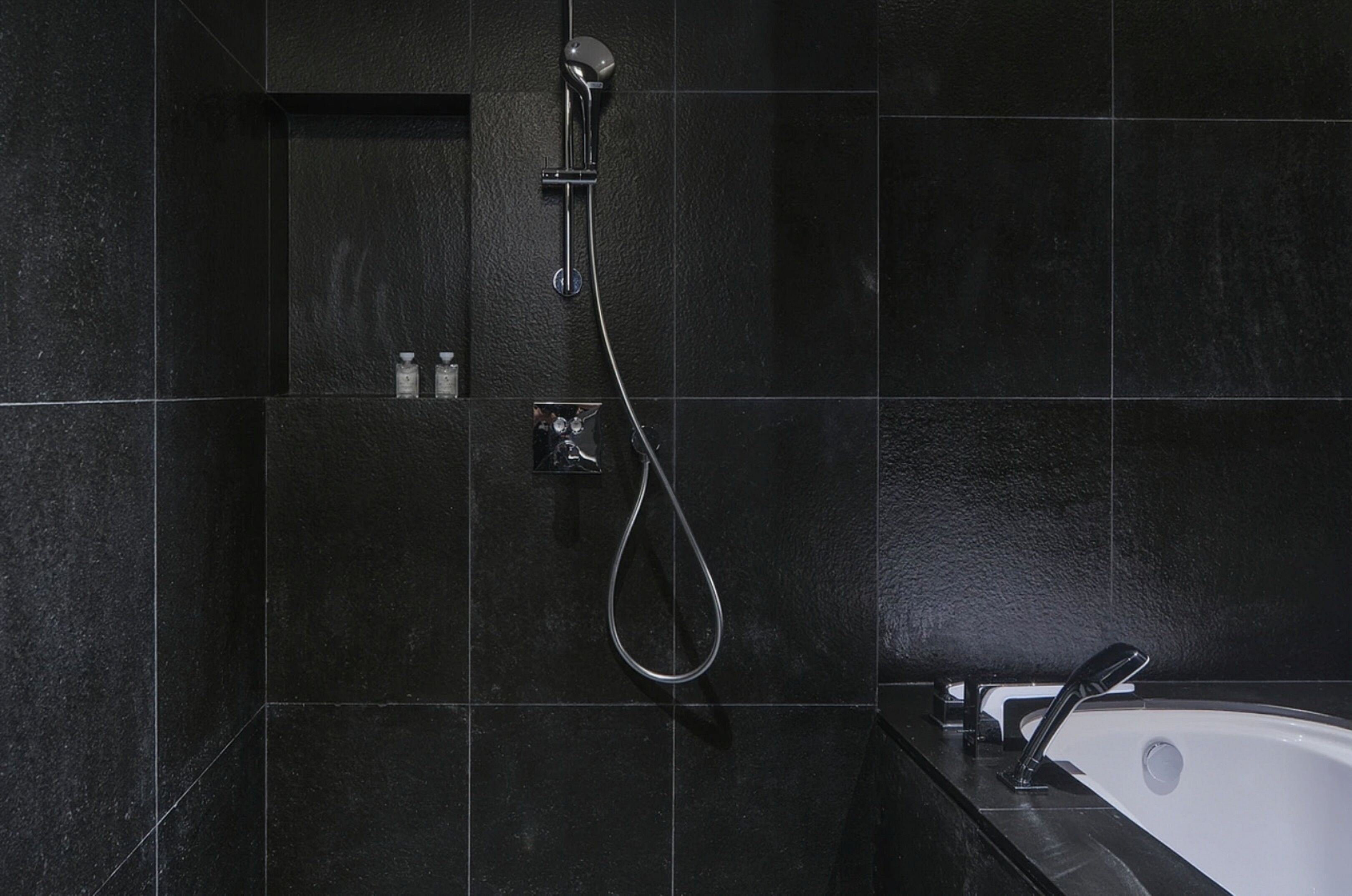 A modern bathroom with dark tiles, a shower, a bathtub, and a faucet.