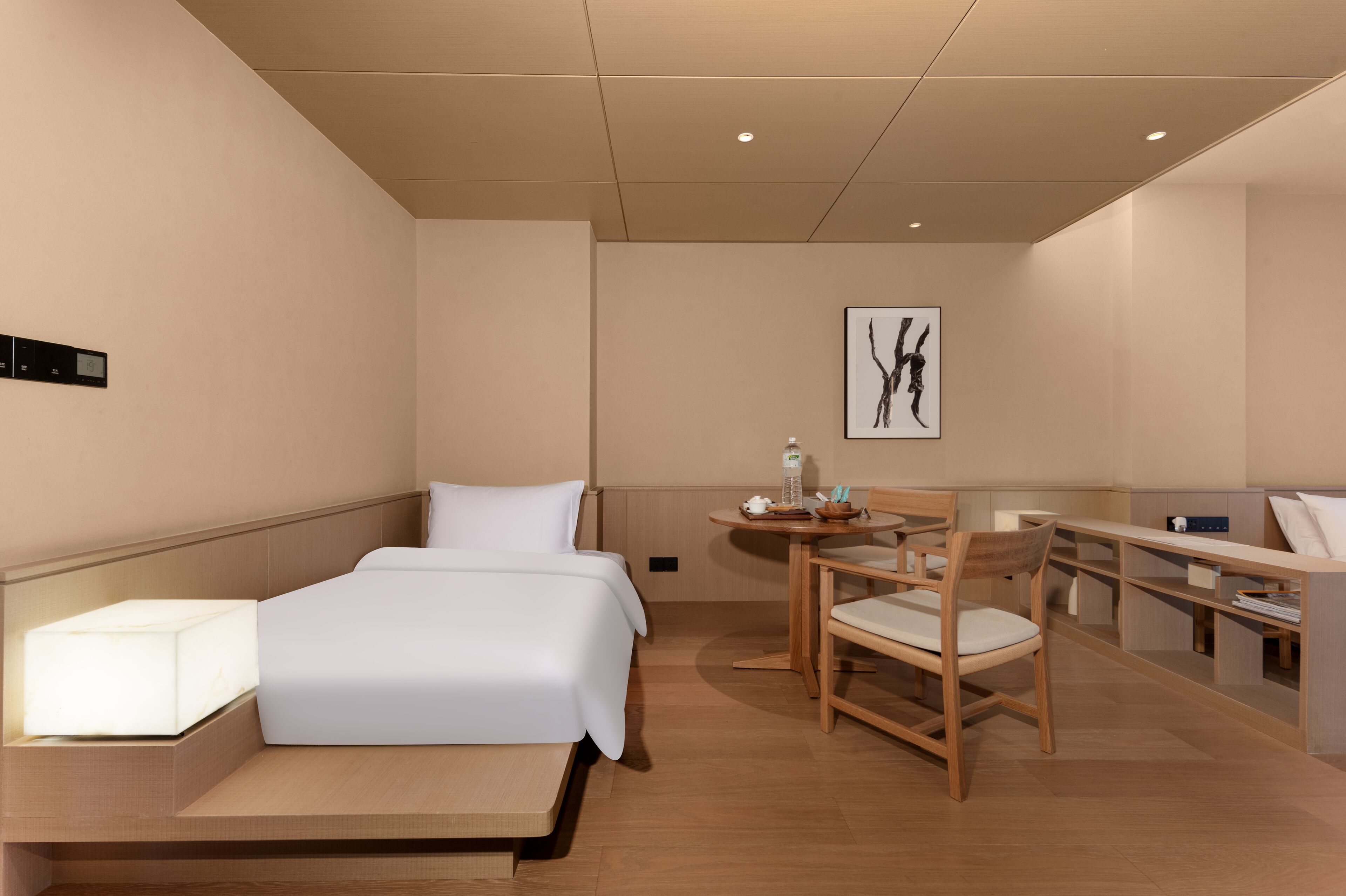 A hotel room with a bed, bedside table, chair, and a desk with a chair.
